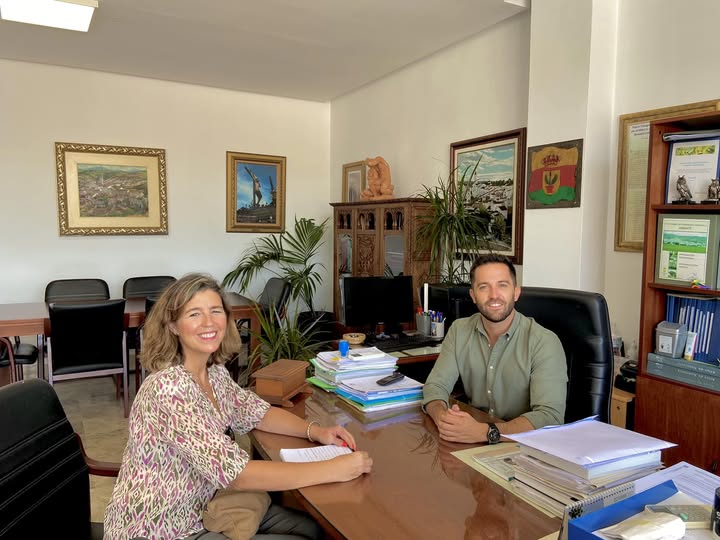 Dos personas en una reunión en una oficina arreglada con decoraciones y plantas.