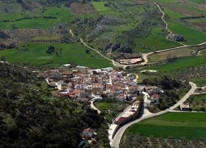 Vista aérea de un pequeño pueblo rodeado de campos verdes y caminos rurales.