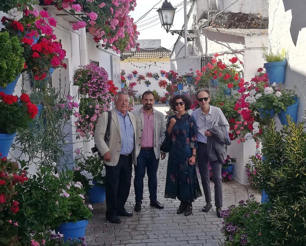 Cuatro personas posan en una calle de pueblo andaluz, rodeadas de macetas azules con flores coloridas.